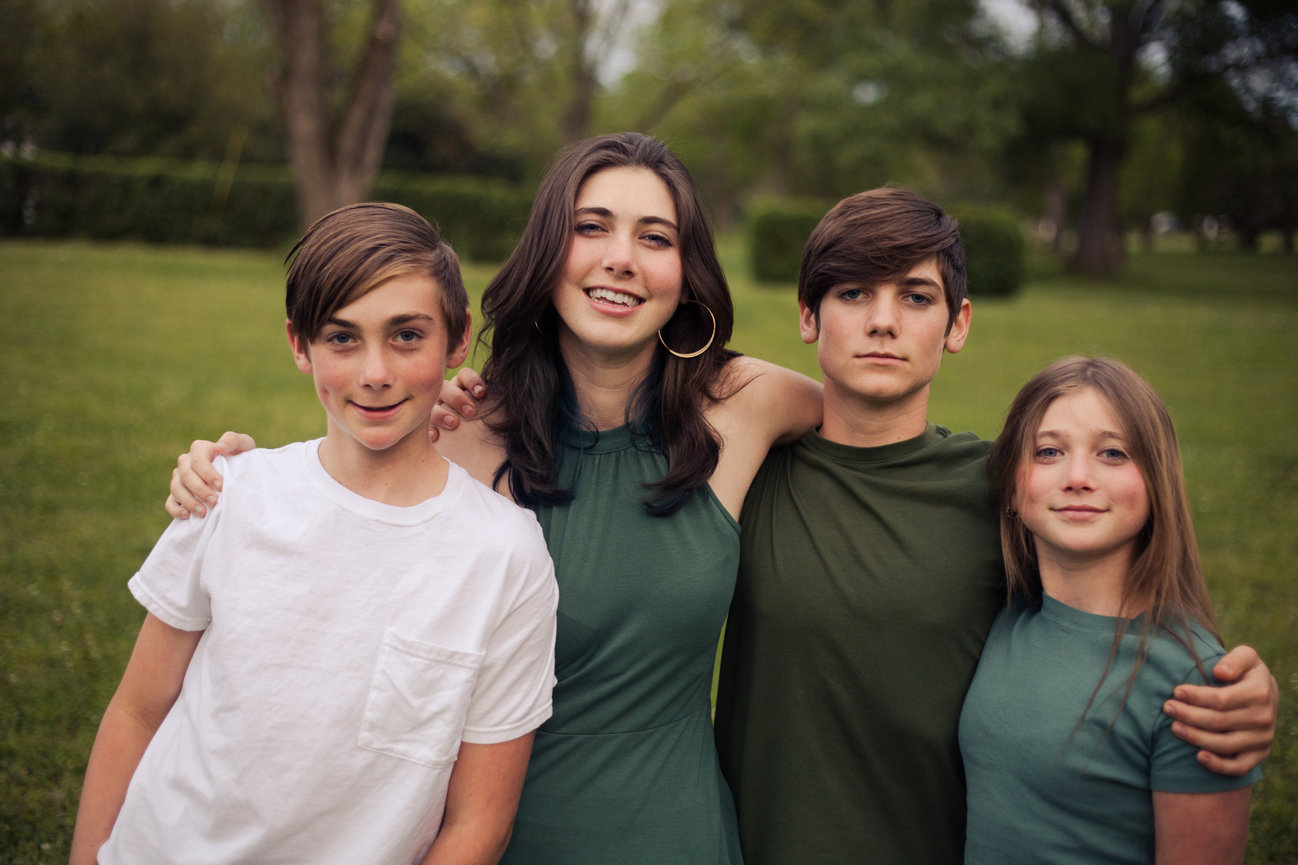 Four siblings posed together outdoors in matching green and neutral tones.
