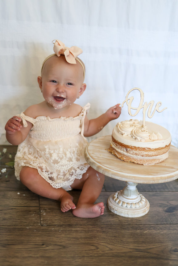 Smiling baby sitting beside a first birthday cake