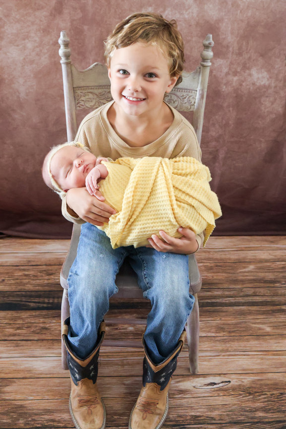 Smiling young child holding a newborn baby on a chair