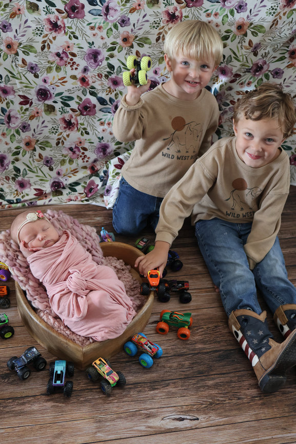 Two children sitting on the floor with a newborn baby and toy cars