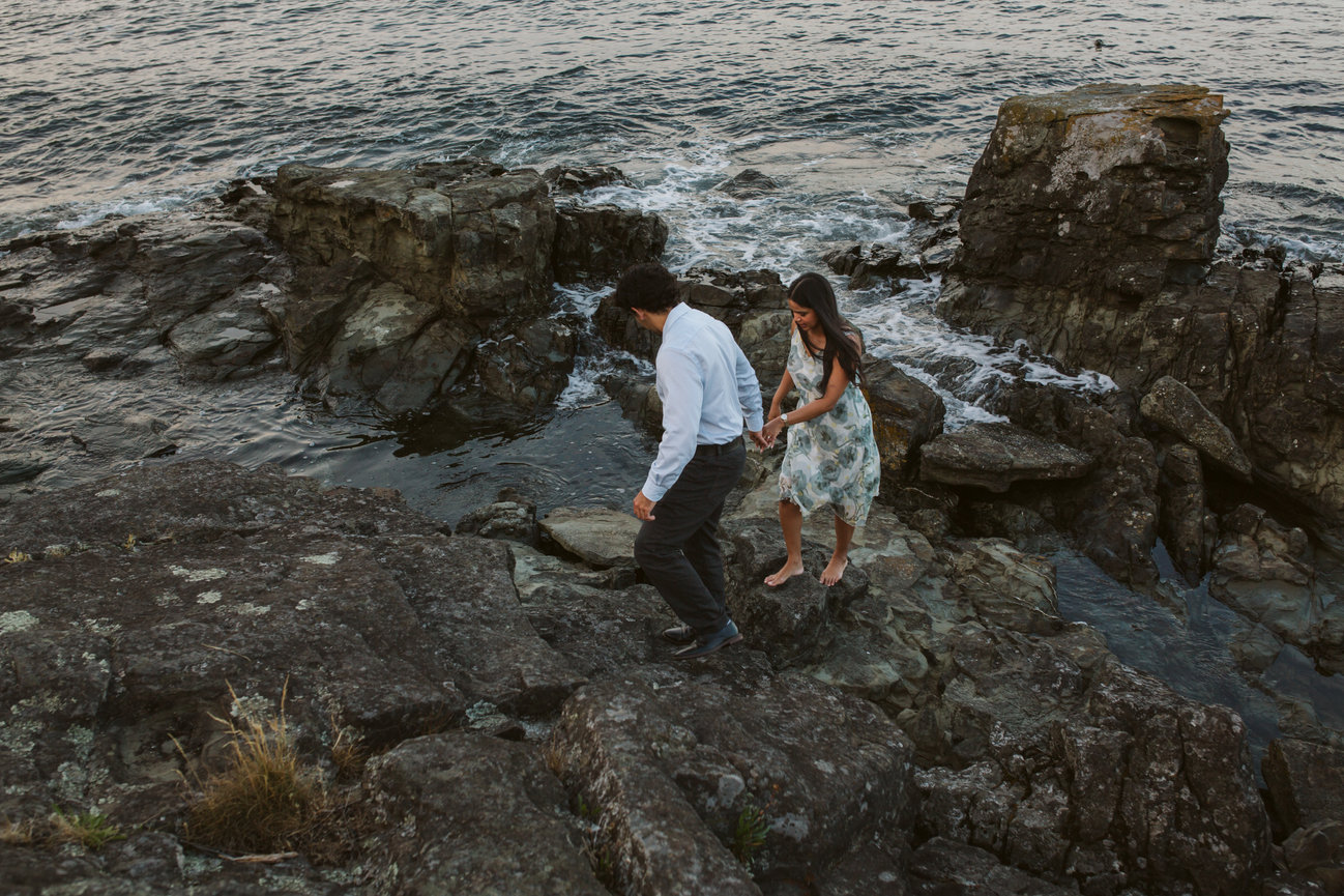 Couple holding hands while walking across shoreline rocks