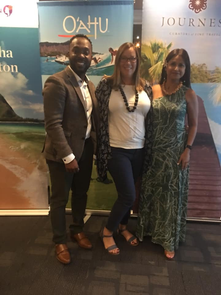 Kelly Furtado and a man and a woman at a travel conference, they are standing in front of a banner that says o'ahu in white lettering