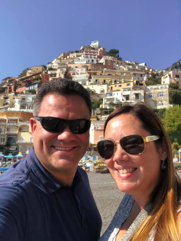 Kelly Furtado and her husband traveling overseas, Kelly and her husband are wearing sunglasses, there are buildings on a hill in the background