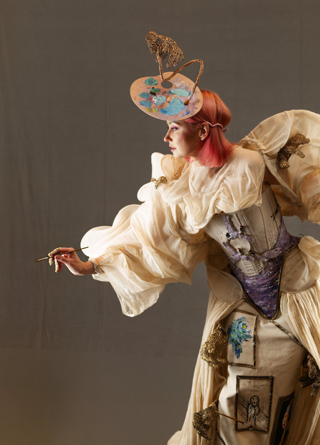 Model in avant-garde attire and hat posing against a plain background
