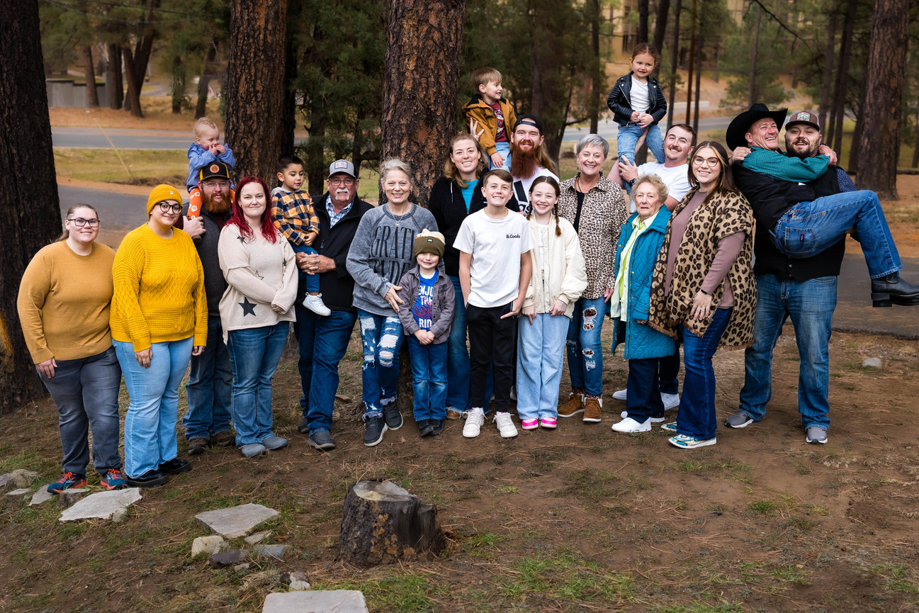 Extended family portrait session outdoors in Ruidoso, NM, featuring a large group of 20 family members of all ages, gathered together in a wooded area.