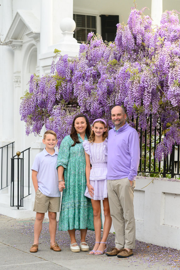 family of four posed in front of a white building and spring wisteria overhead