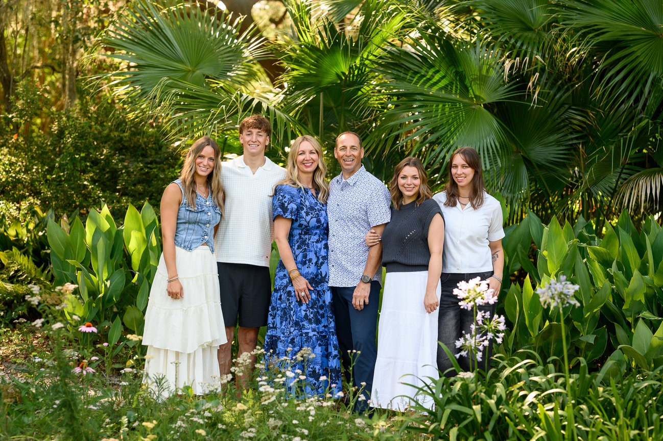 family of six adults standing posed in a garden surrounded by flowers and green palms