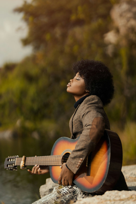 Woman with guitar sitting by lake