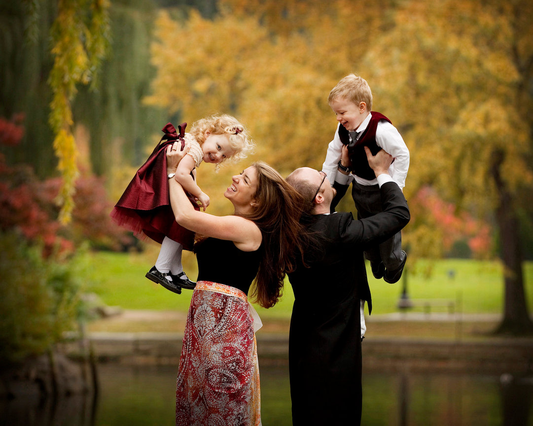 Family playing together in a park with autumn trees, adults holding children in the air