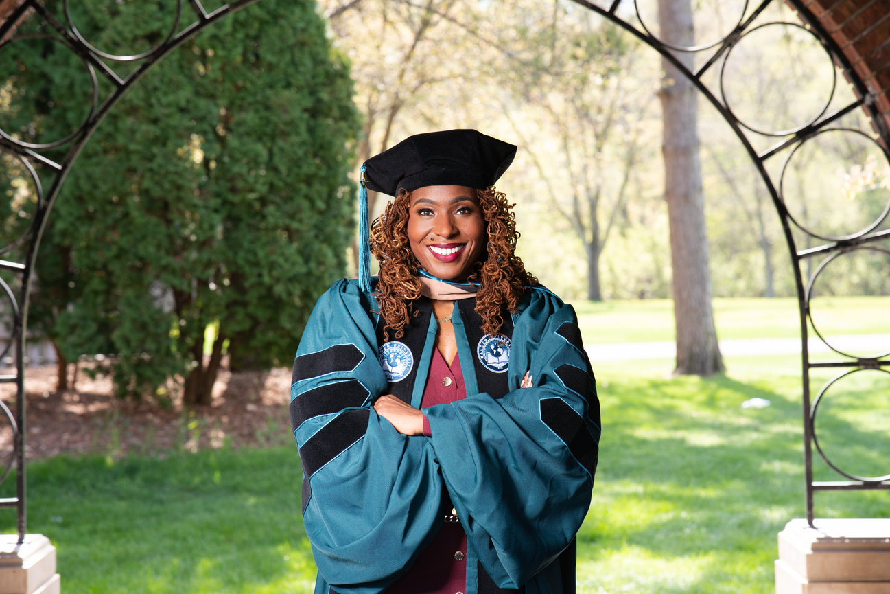 Smiling graduate in cap and gown standing outdoors under an archway