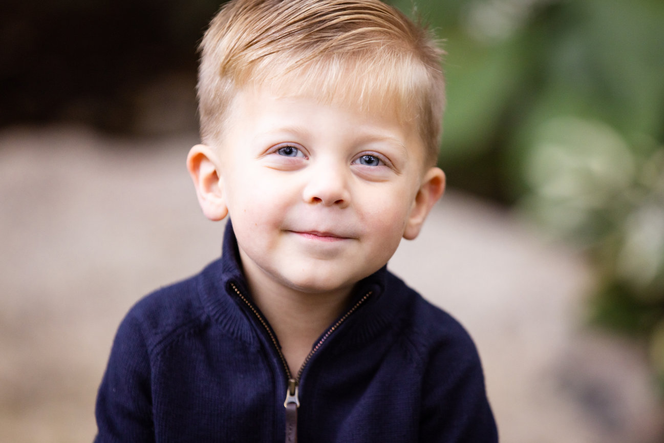 Cute toddler boy in a blue shirt, looking at the camera with a sly smile.