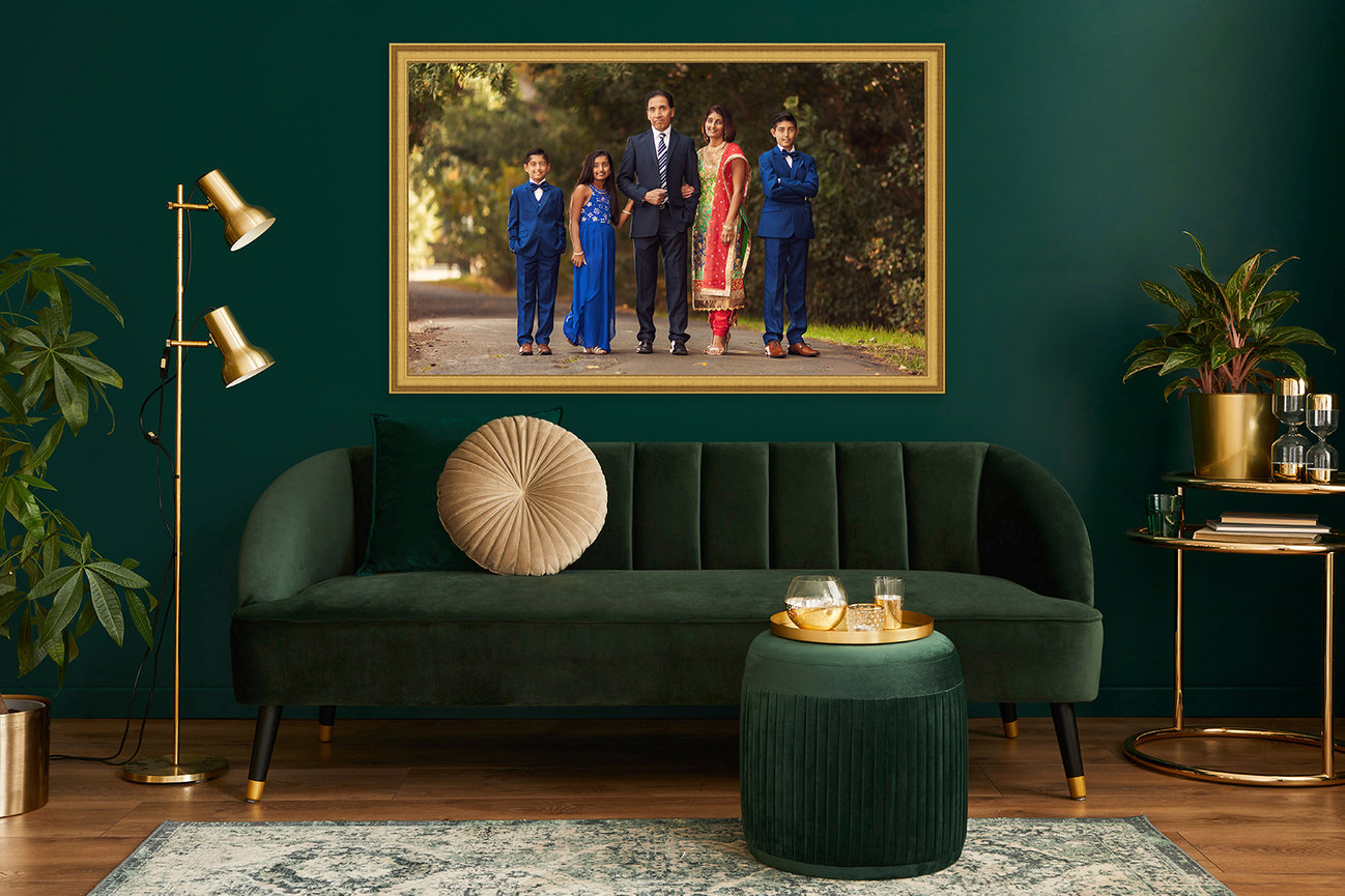 Elegant living room with a green sofa, gold accents, plants, and a family portrait on the wall.