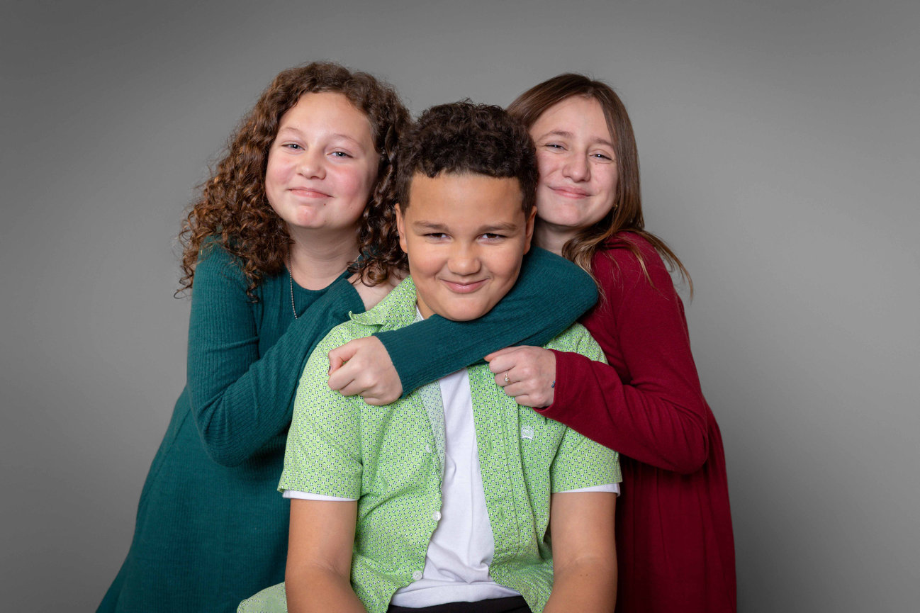 Three smiling children posing close together against a gray studio background in Blue Springs photographed by Case Studios Photography