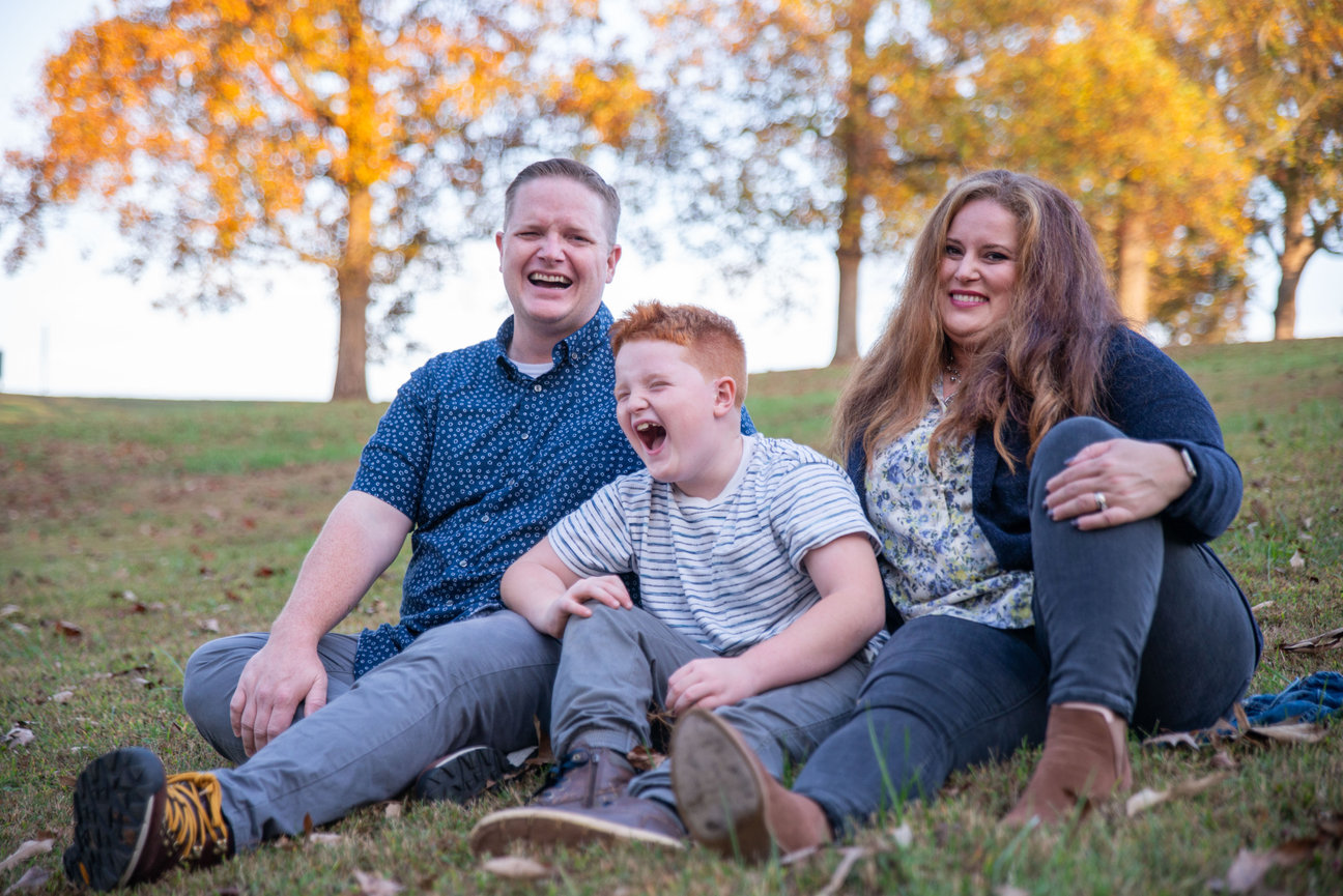 Family sitting on the grass with colorful autumn trees behind them.