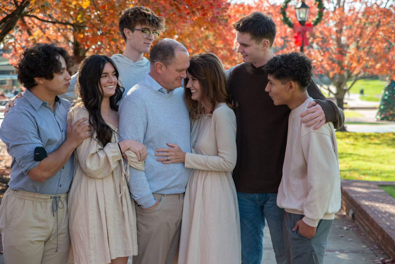 Extended family standing together outdoors with autumn leaves behind them.