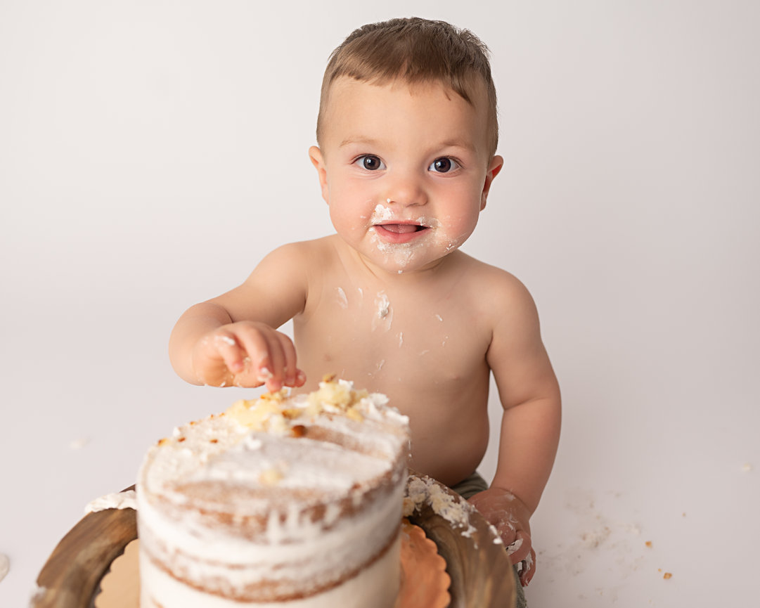 Baby boy smashing cake in Shrewsbury with frosting on face on white backdrop