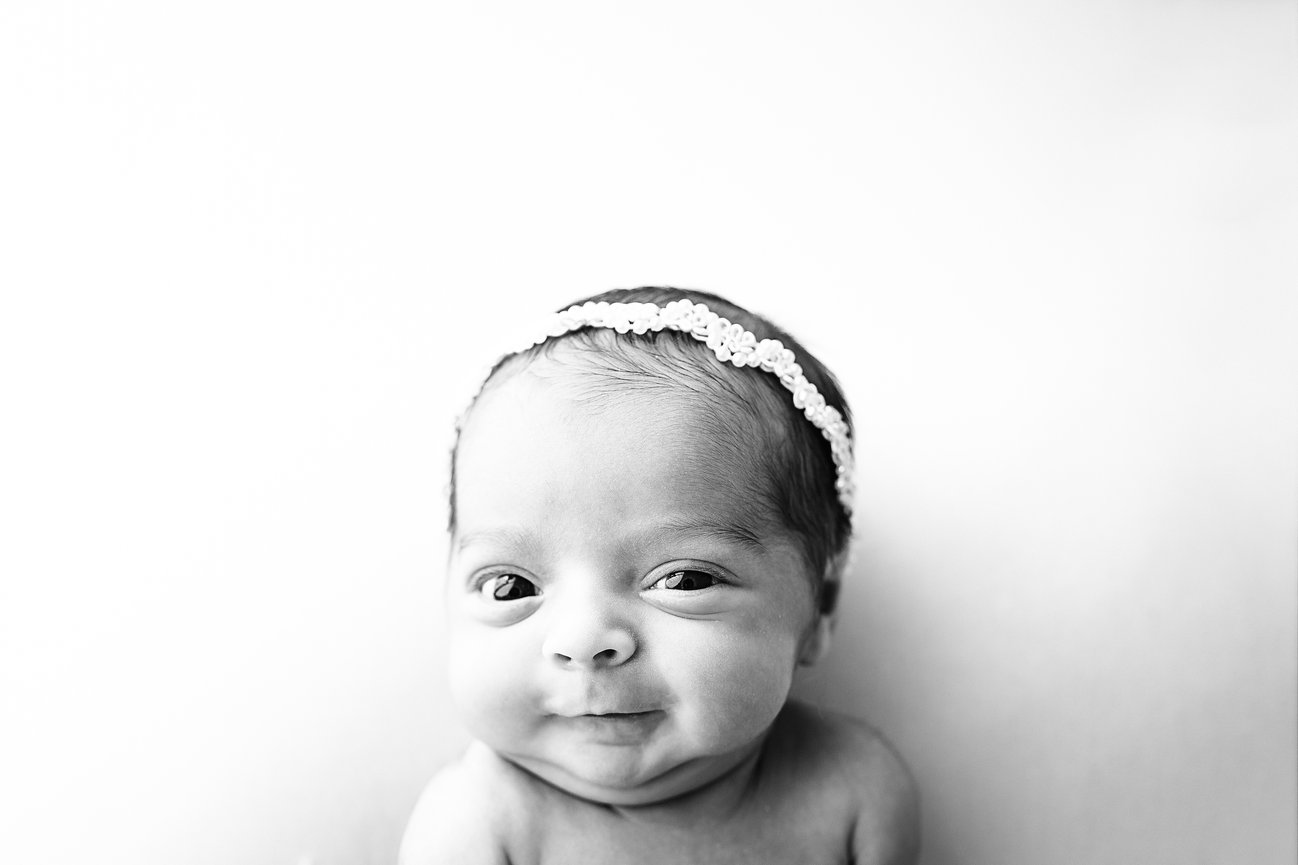 Black and white photo of newborn smirking at one week old, showcasing sweet and silly moments in studio