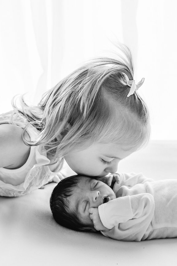 Emotional image of young toddler kissing baby during a baby-led newborn session in Kristin Baker’s Manasquan studio