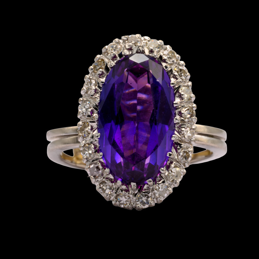 Elegant ring featuring a large oval-cut deep purple amethyst surrounded by a halo of round brilliant-cut diamonds, set in a split-shank white gold band, displayed against a black background