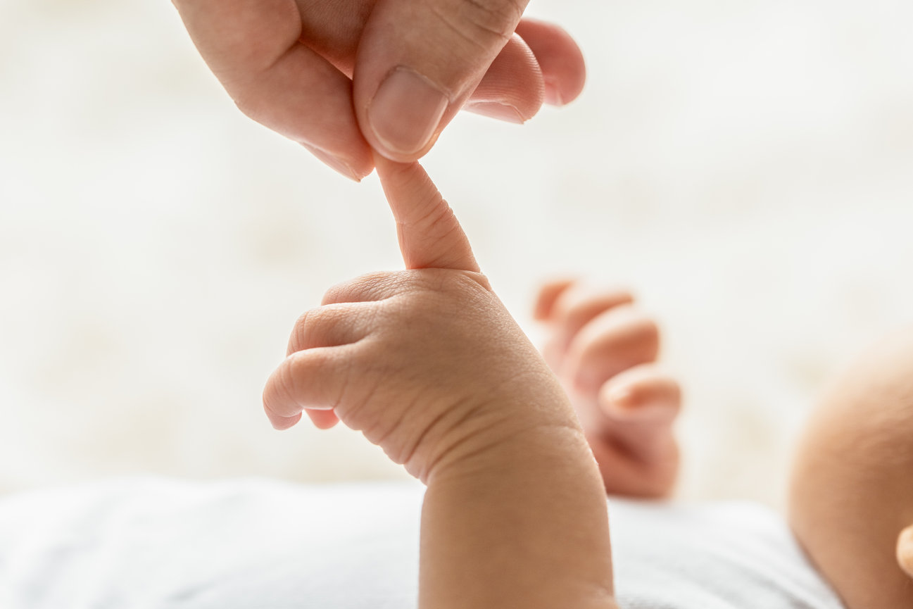 Adult holding a baby's hand gently, conveying care and connection.