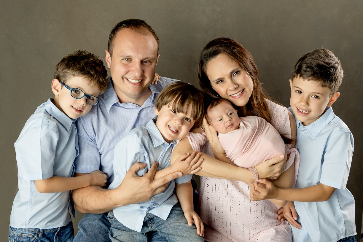 Family of six including newborn posed in winnipeg studio against beige backdrop wearing blue and pink