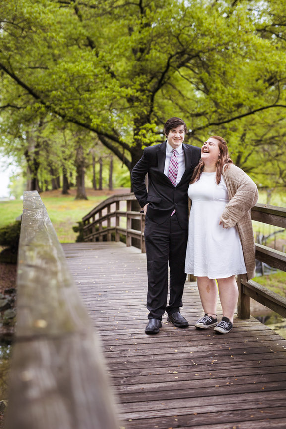 Young couple laughing on a wooden bridge surrounded by greenery.