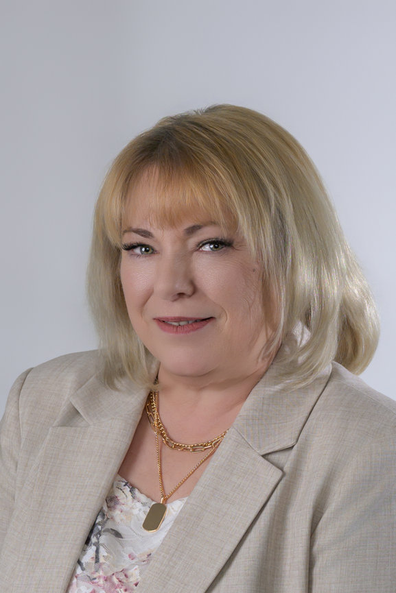 headshot of woman in light color tan blazer and floral blouse with blonde hair slightly off center looking at camera with slight smile