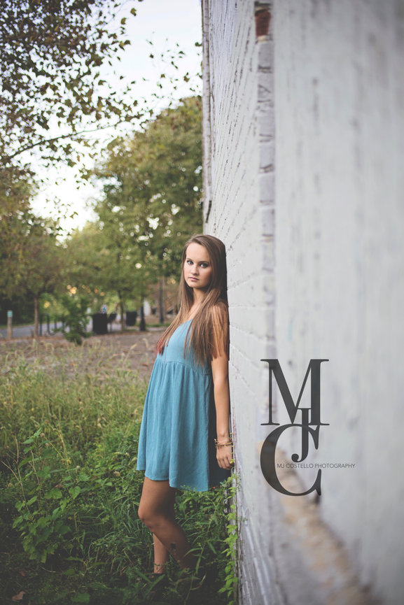 Young woman in a blue dress leaning against a white wall outdoors