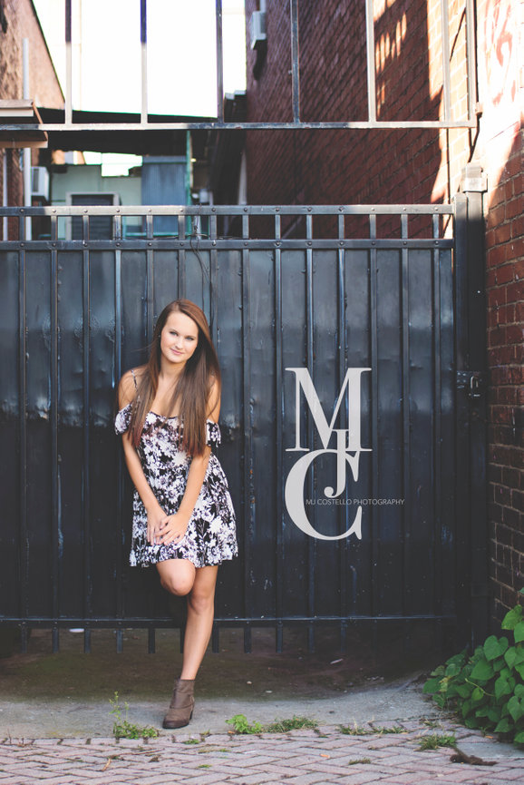Young woman posing in a floral dress in front of a dark industrial wall