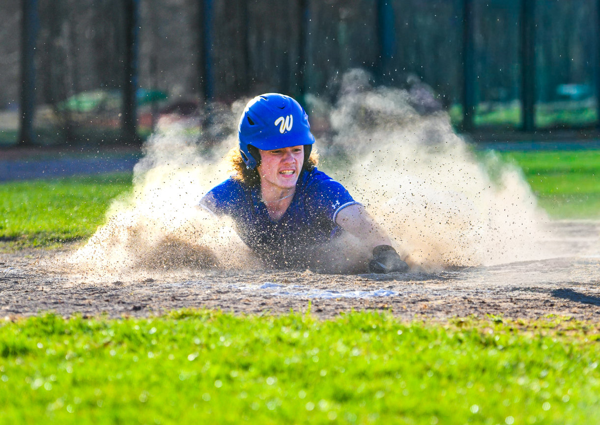 A baseball player slides through dirt on a wet field during a game.