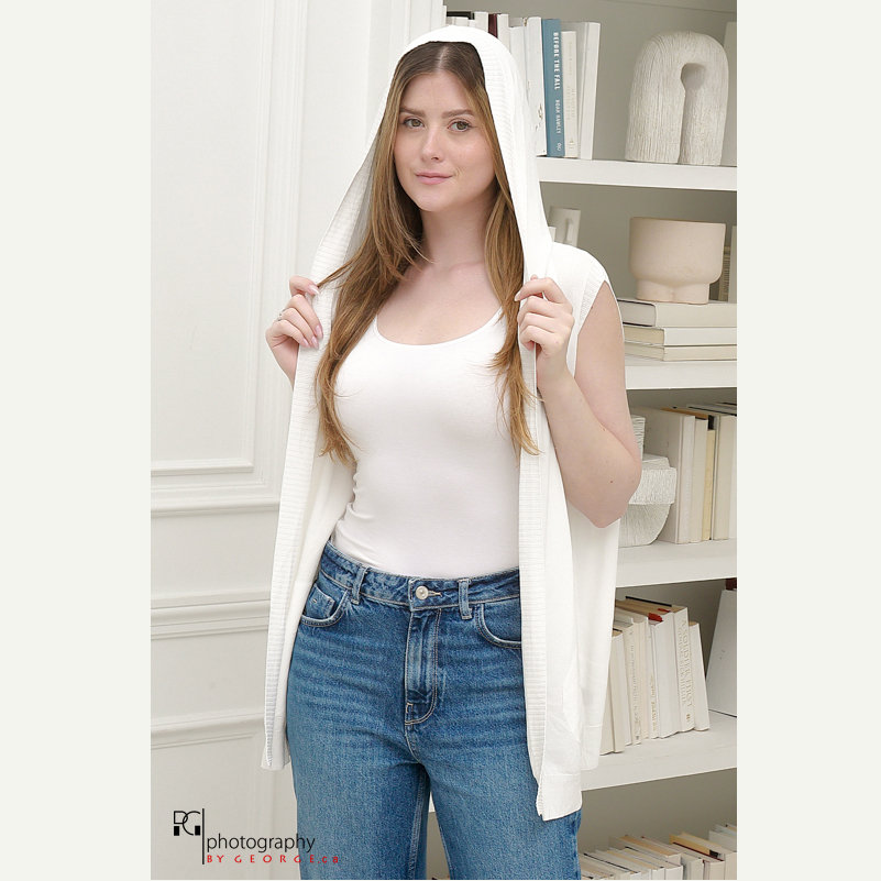 Model wearing white hooded vest over tank top with blue jeans in modern studio fashion photoshoot.
