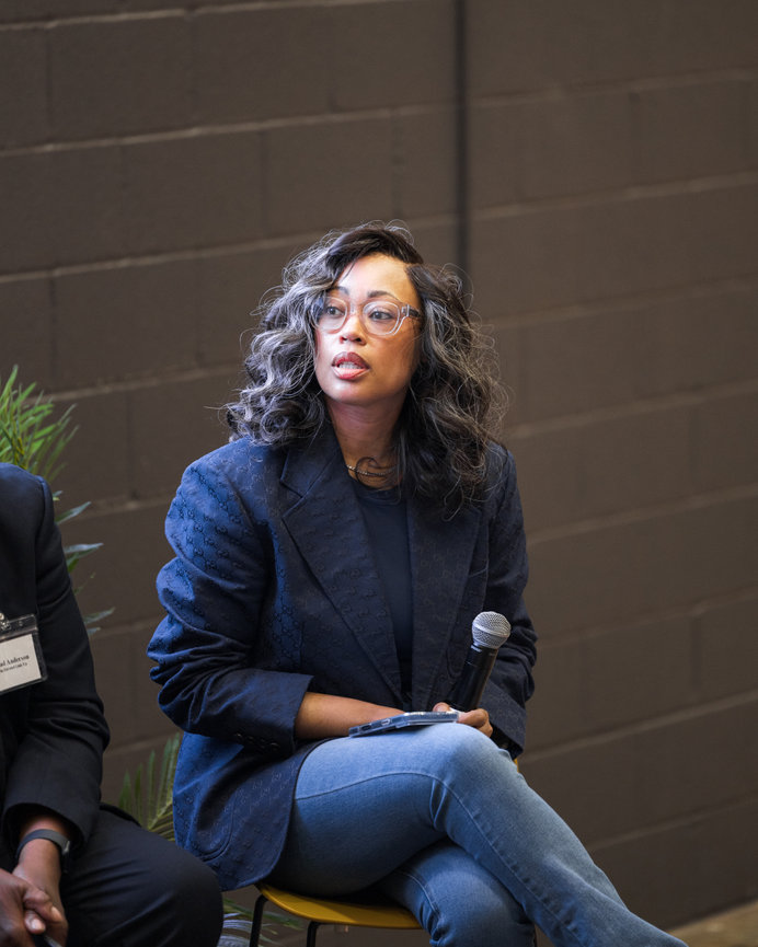 Event photography of a woman with curly hair and glasses speaking into a microphone at an Atlanta event