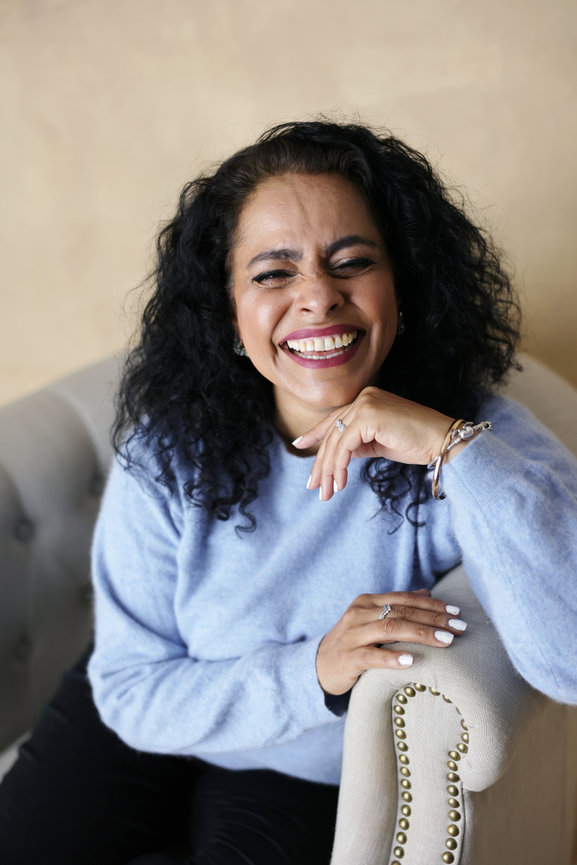 Smiling woman with curly hair sitting on a chair in a light blue sweater. authentic photos for my business and website