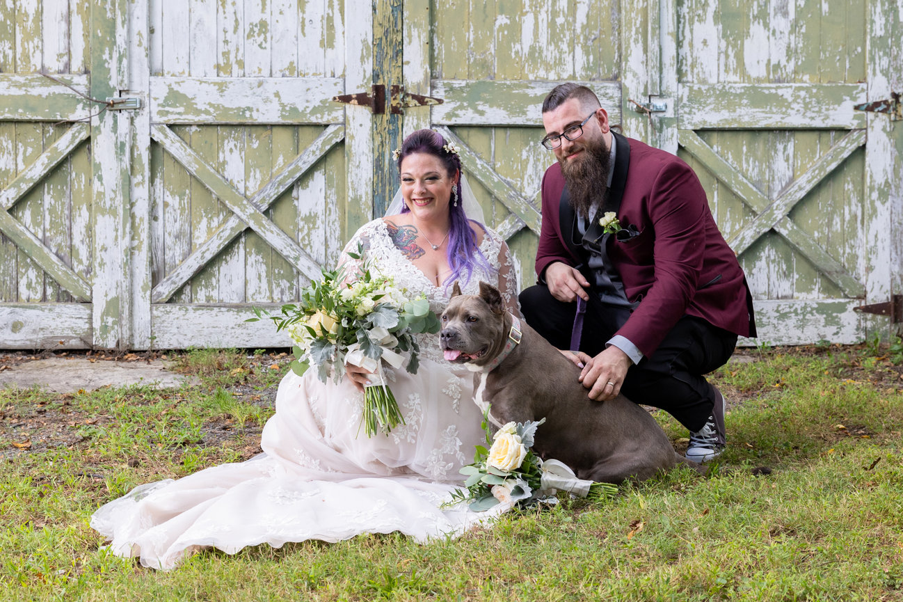 Bride and groom with their dog in front of rustic barn doors