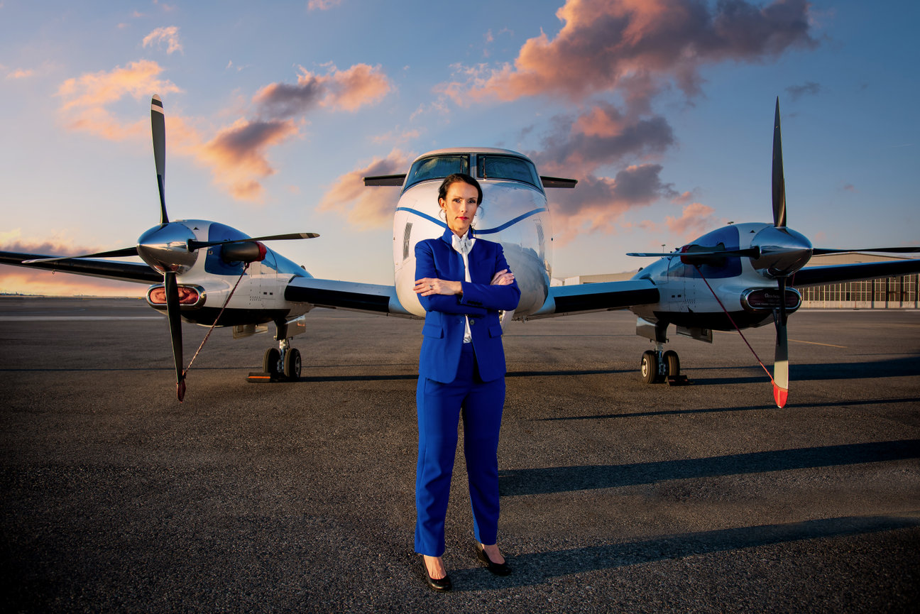 A woman wearing a blue suit posing in front of a private plane.