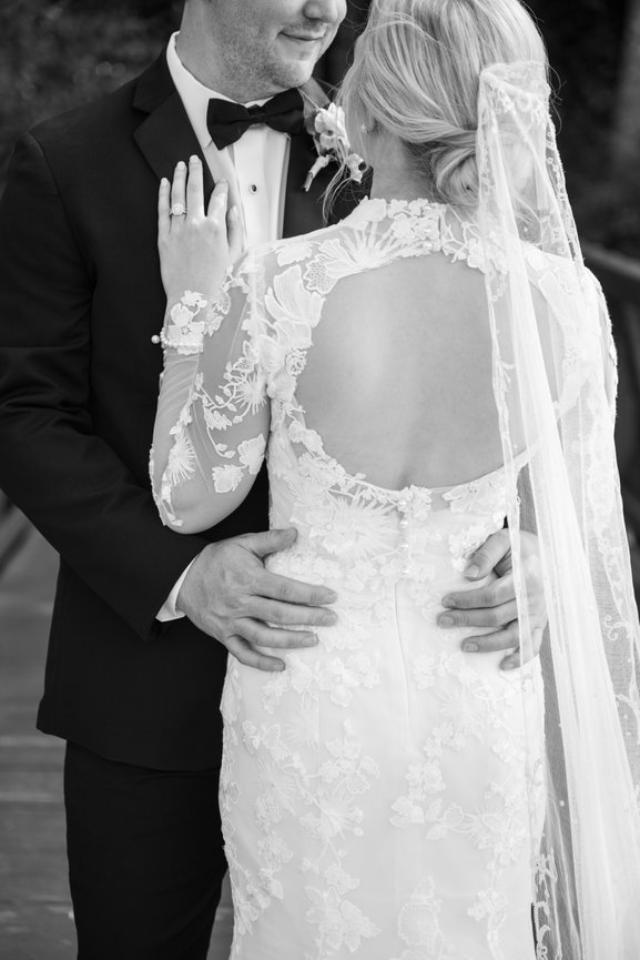 Bride in lace Monique Lhuillier wedding gown standing with back to the camera facing her groom. High Hampton wedding photography by Heather Durham.