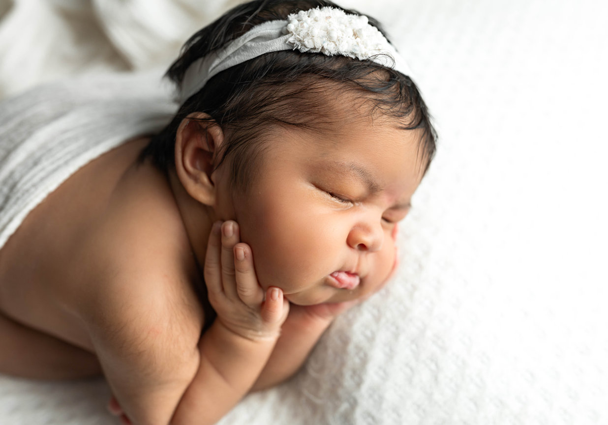 Newborn baby with headband propping head up in newborn photo session
