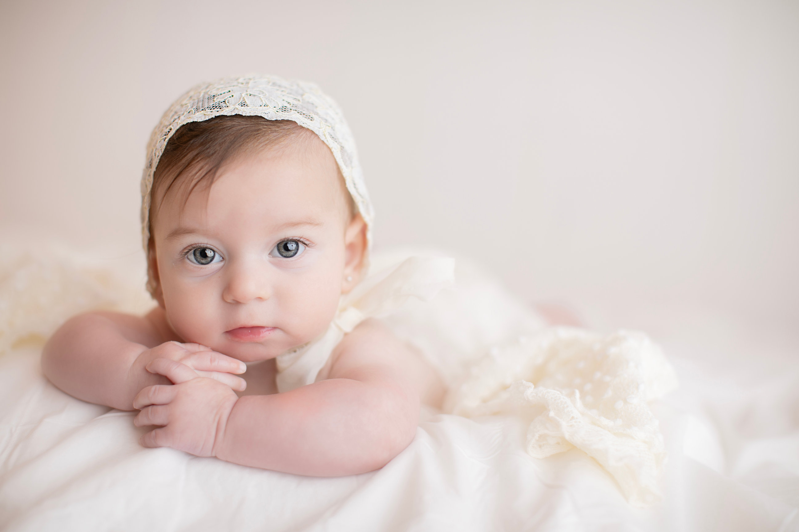 Baby resting their chin on their hands on a cream blanket