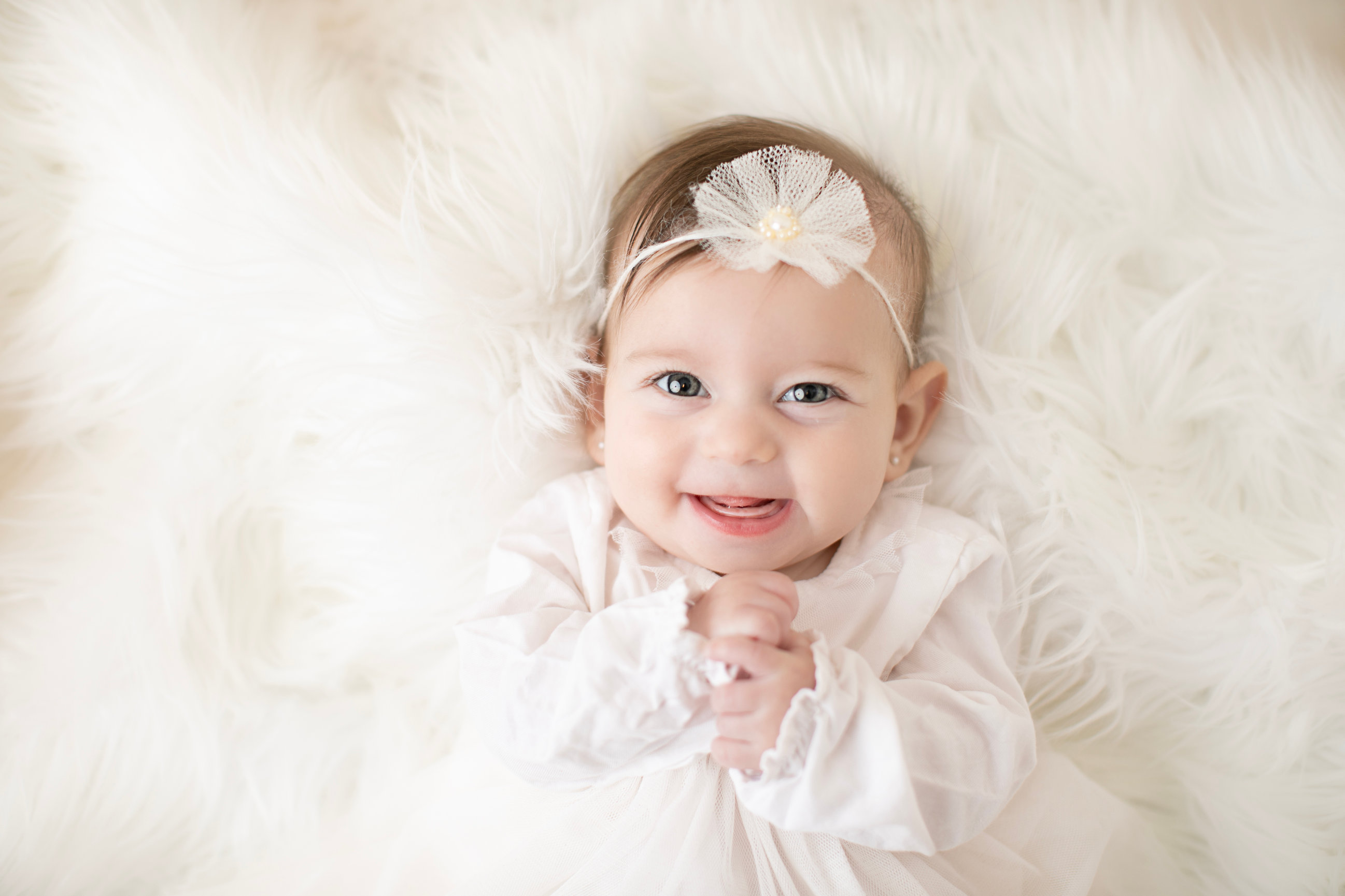 Baby wearing a white outfit and flower headband on cream fur