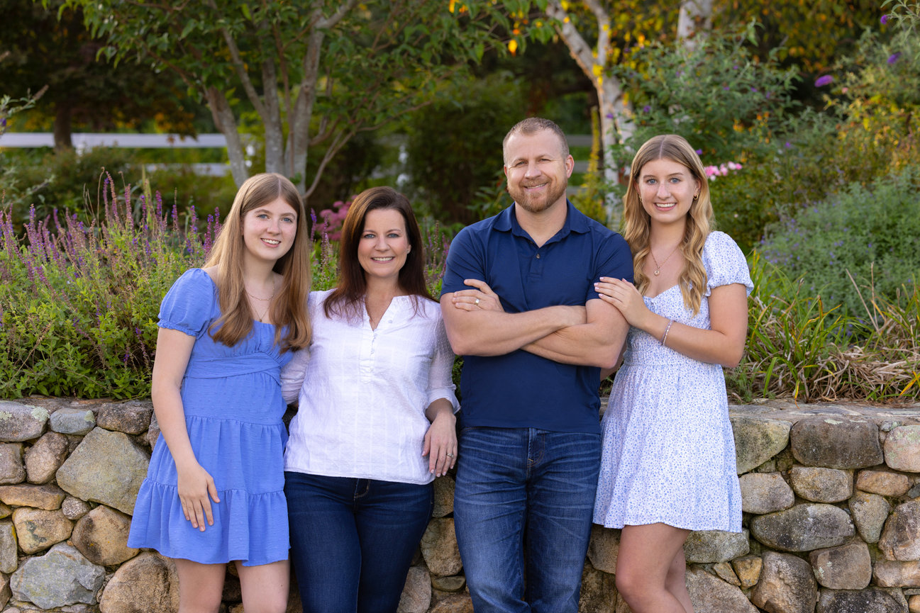 outdoor family portrait of parents with twin high school senior girls by stone wall and garden in blue