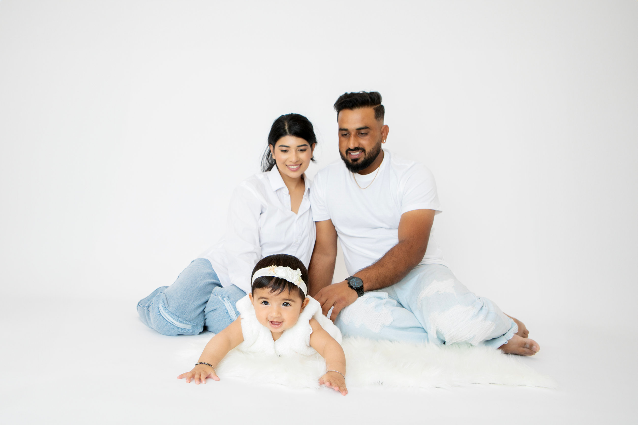 Parents in white sitting behind their baby in the studio
