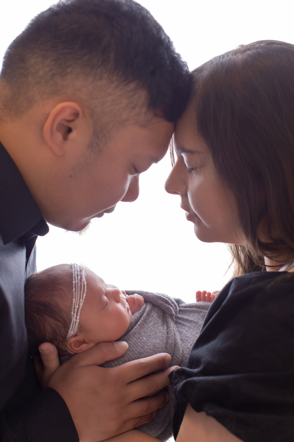 Parents forehead to forehead holding their sleeping newborn daughter