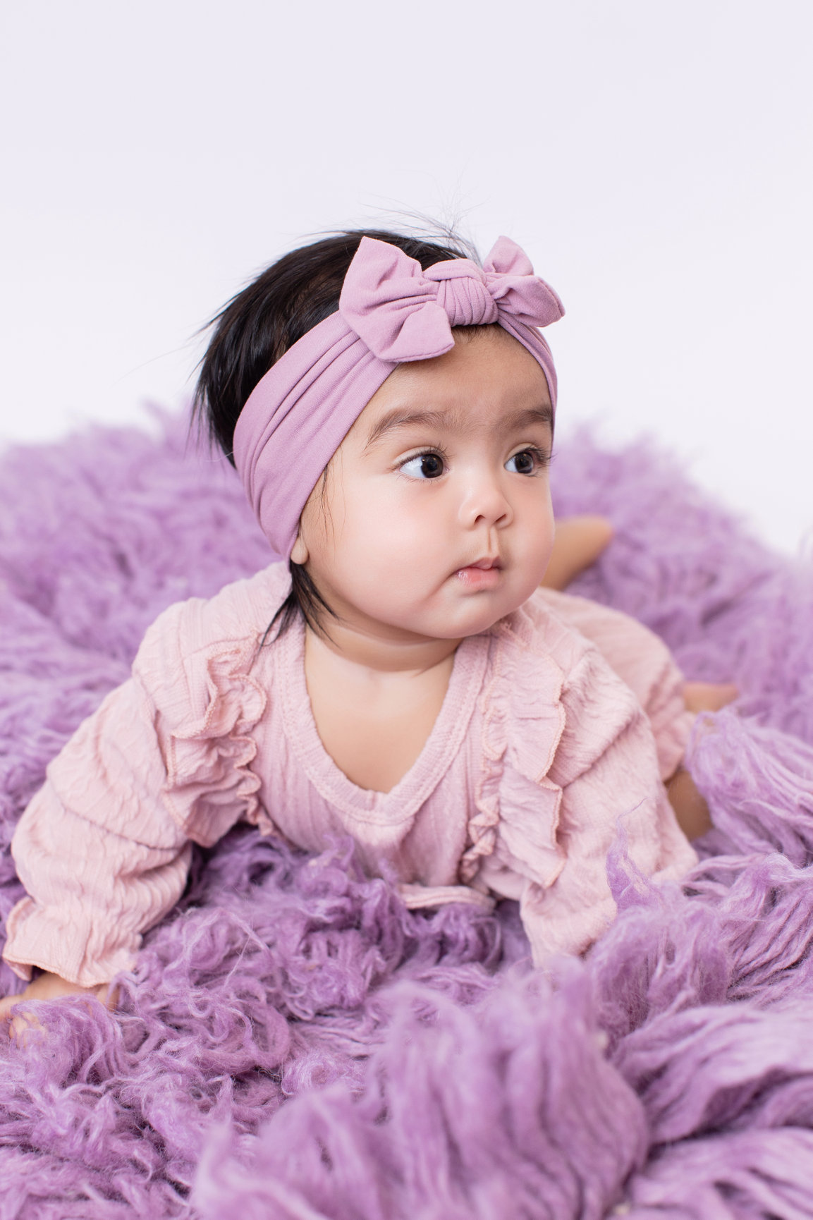 Baby wearing a dusty pink romper on lilac fur