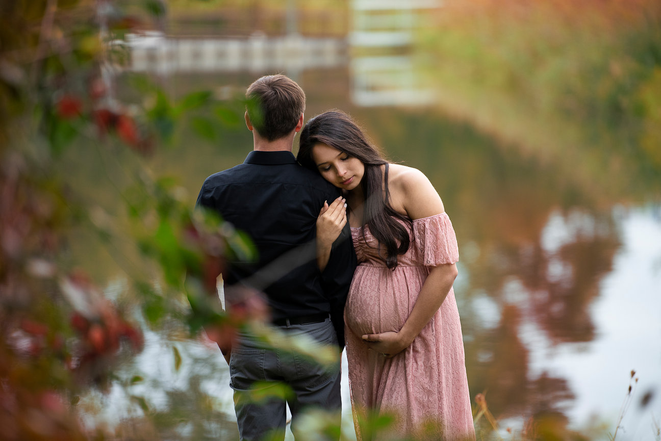 softly on the shoulder of a man in a black shirt by a serene lake. The background features blurred autumn foliage, creating a peaceful and intimate atmosphere.