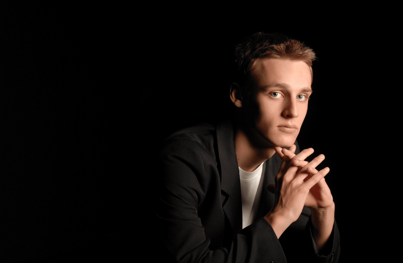 A senior boy in a sharp black blazer rests his chin in his hands.