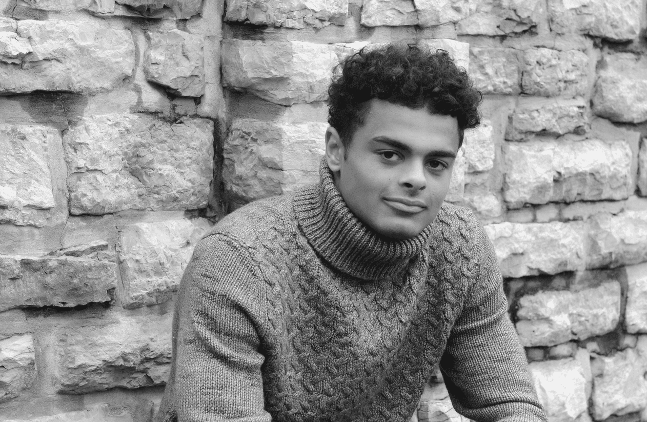 Haven wearing a timeless corded sweater sitting against a stone wall on campus of the University of Iowa..