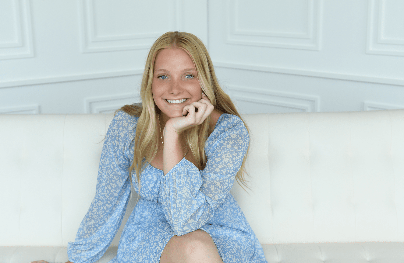 A bright spirited teenage girl in a blue dress smiling widely.