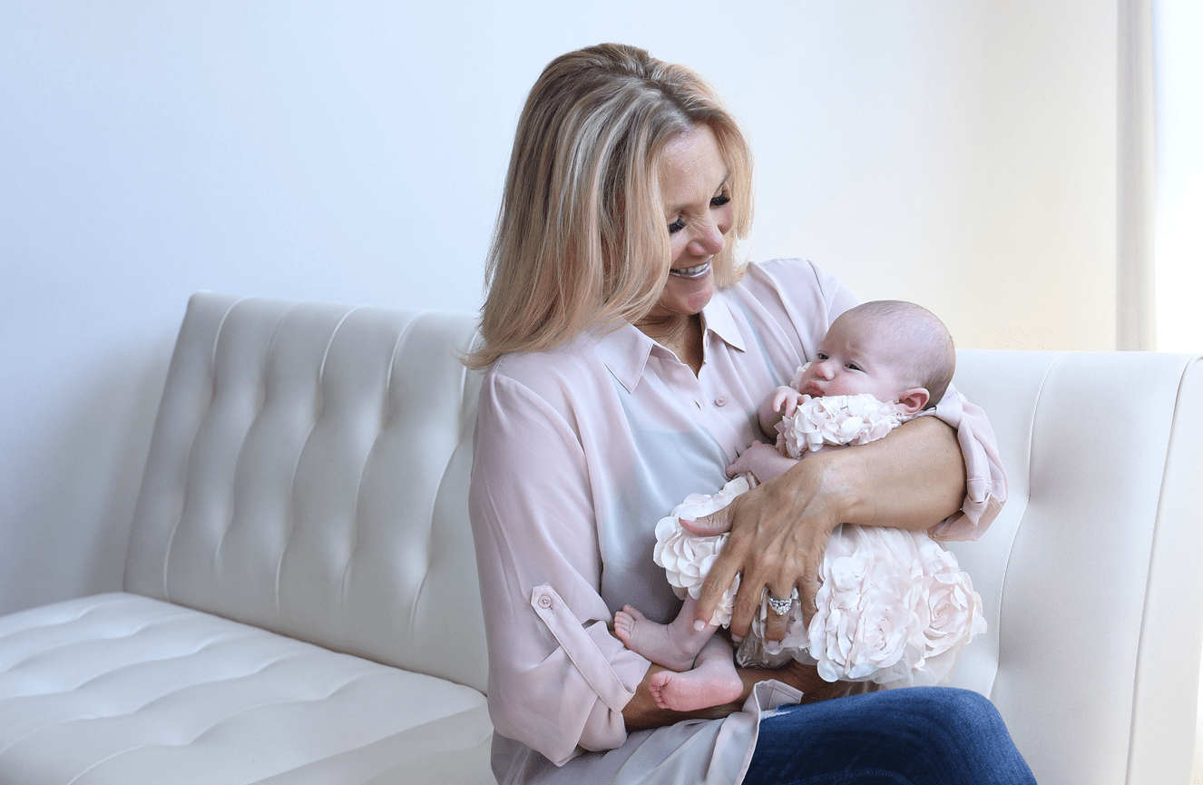 A grandmother smiles down at her granddaughter who is wearing a pink ruffled dress during a family photo session at Kliks Photography.