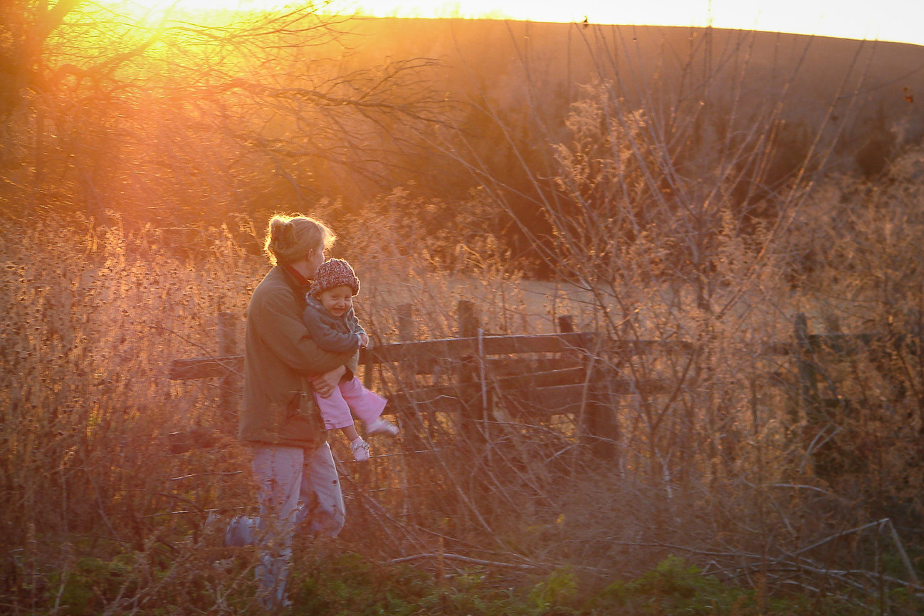 Parent holding child in a field during sunset
