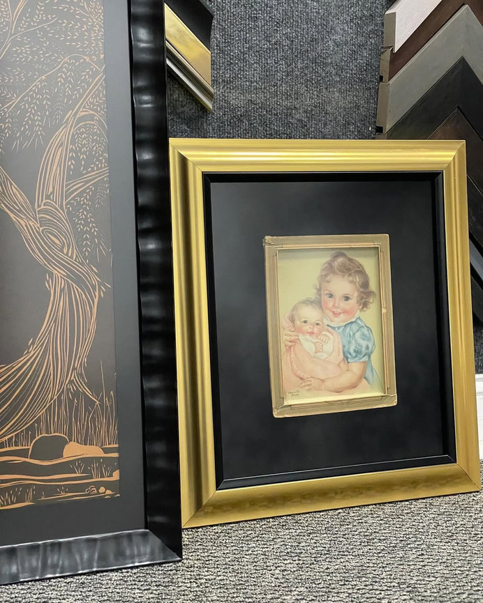 Framed child portrait leaning against a wall beside larger artwork